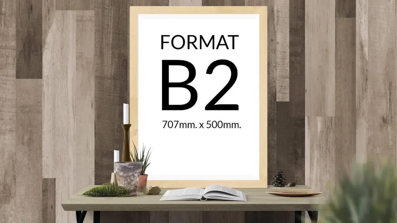 Ramka z napisem "FORMAT B2 707mm. x 500mm." na tle drewnianej ściany. Na stole obok świece, rośliny i otwarta książka.