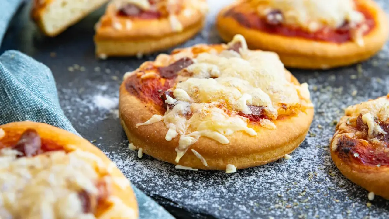 Mehrere mini pizza mit geschmolzenem Käse und Tomatensauce auf einem dunklen Untergrund, bestreut mit etwas Mehl.