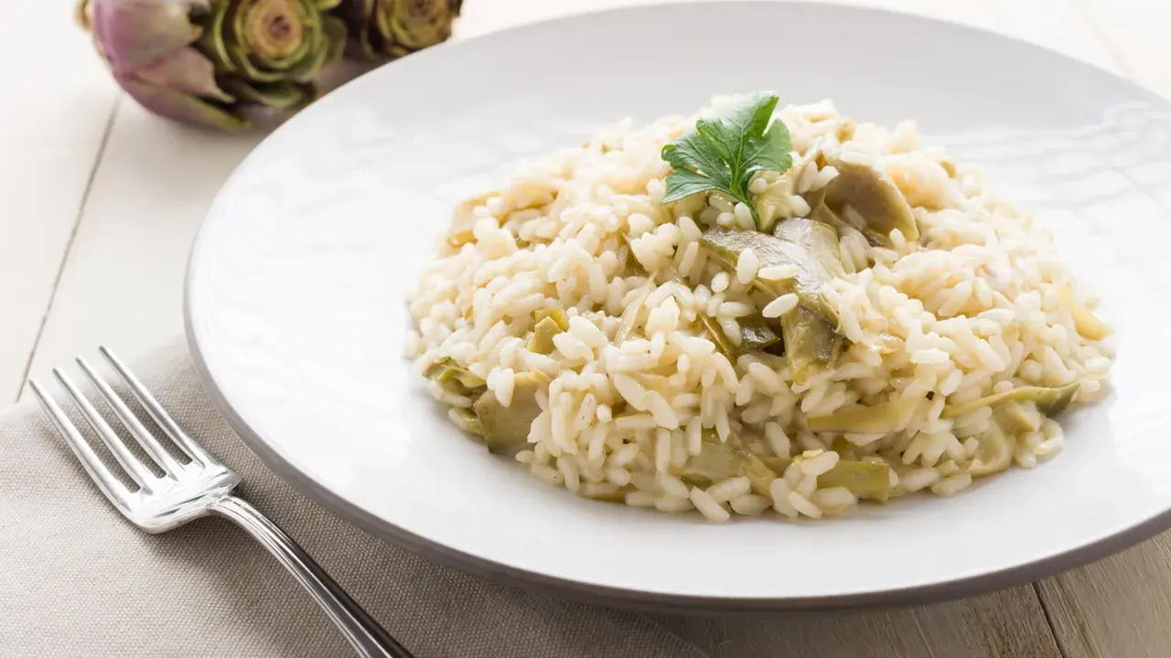 Un cremoso risotto con carciofi freschi, guarnito con un ciuffo di prezzemolo, pronto per essere gustato.