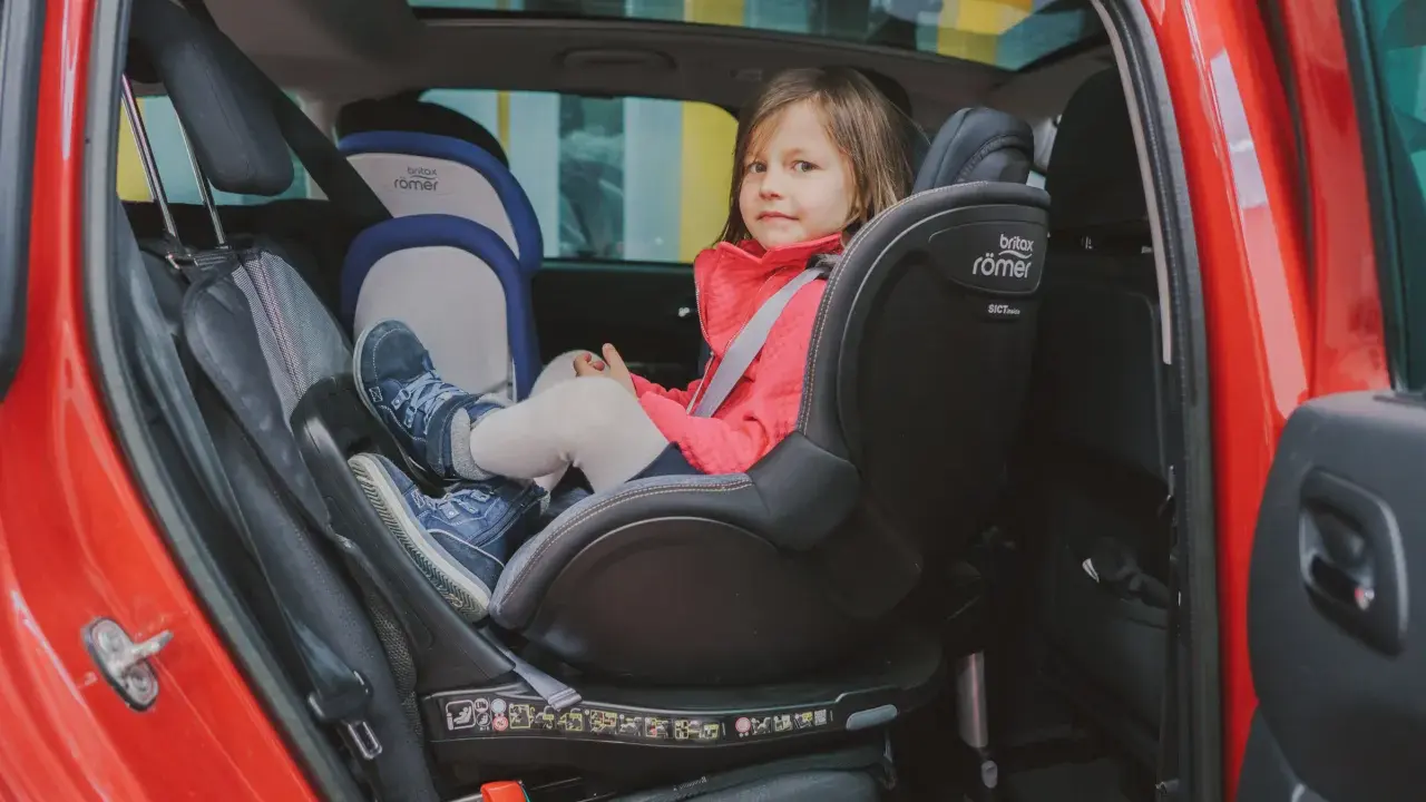 Mała dziewczynka w czerwonej kurtce siedzi w foteliku samochodowym Britax Römer.