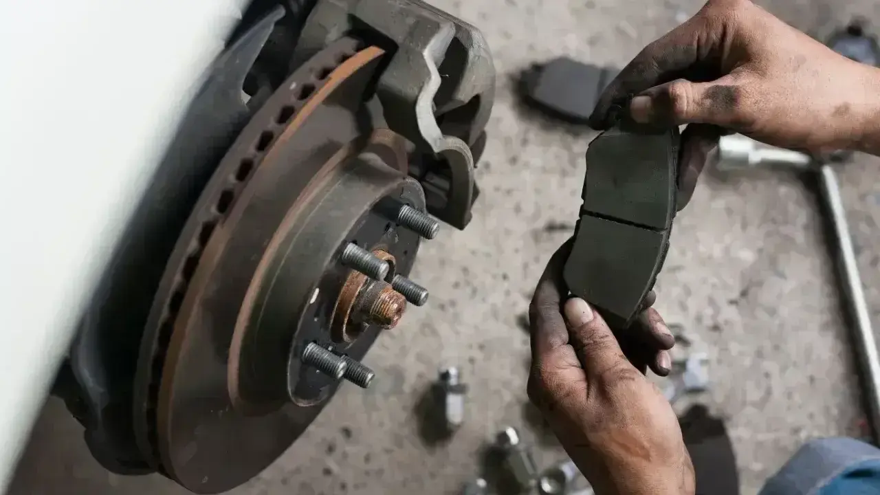 Mechanik trzyma zużyte klocki hamulcowe. Sprawdź wymiana klocków hamulcowych cena i zadbaj o bezpieczeństwo.