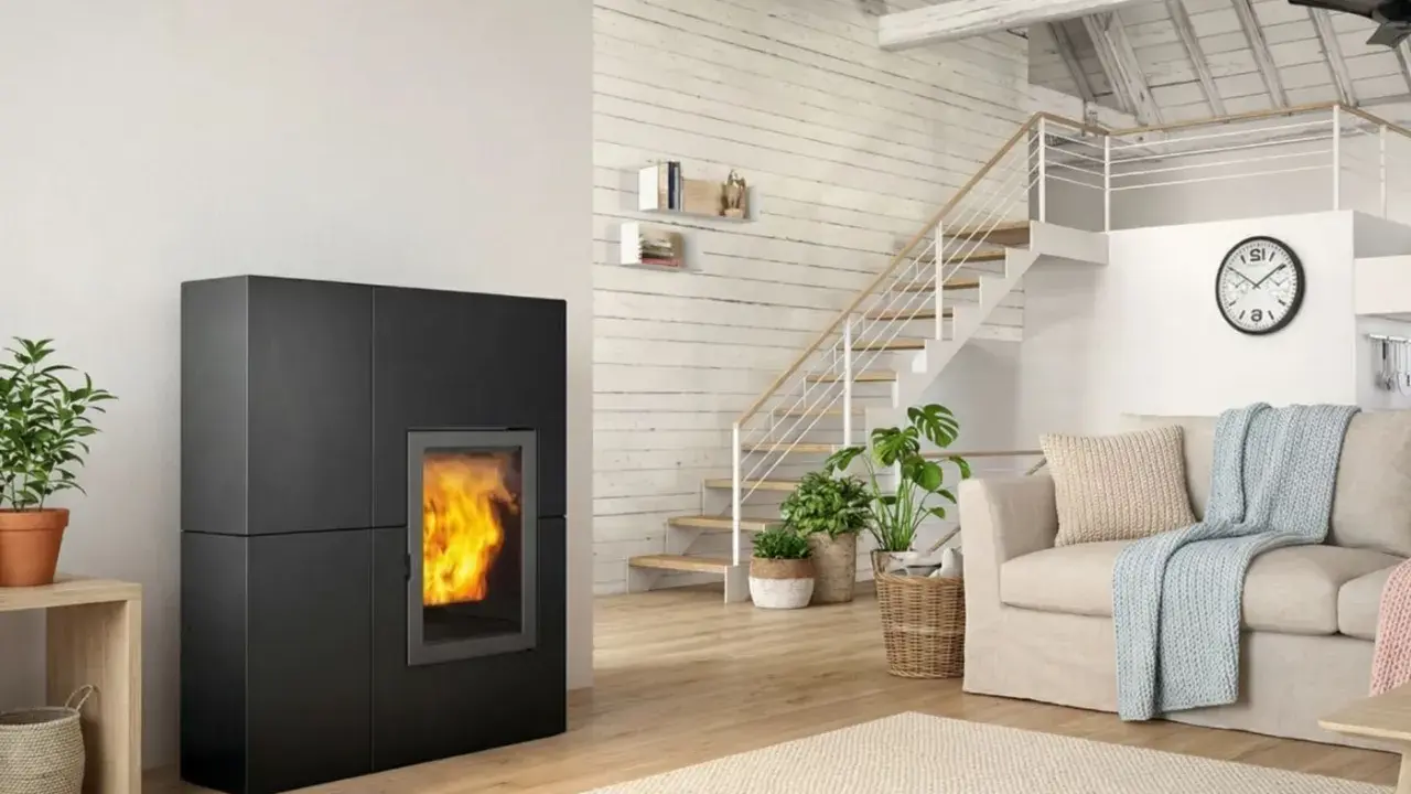 Estufa de pellets negra con fuego encendido, junto a escaleras y sofá. Ideal para un esquema de instalación de hidroestufas de pellets.