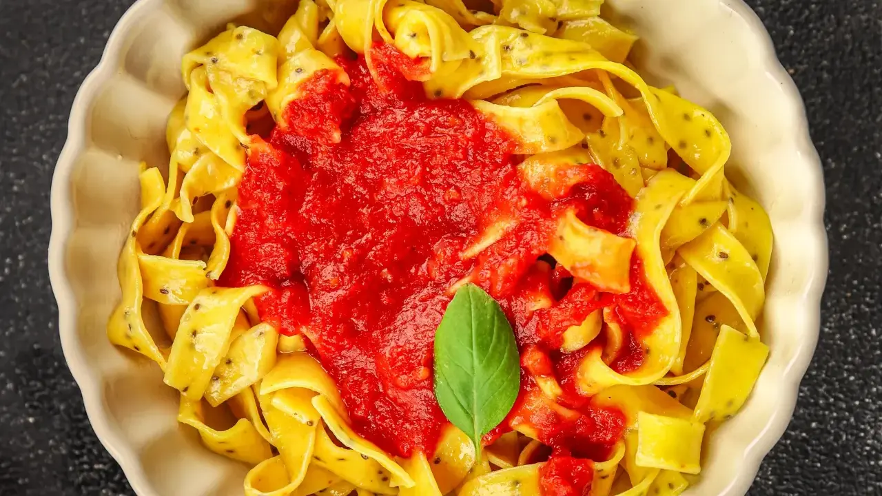 Pappardelle z sosem pomidorowym i bazylią, klasyczne makaron po włosku, podane w kremowej misce.