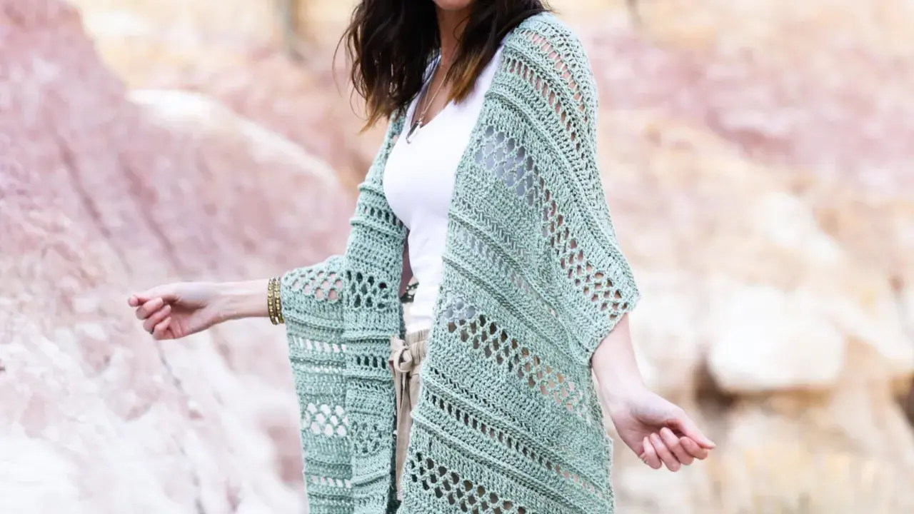 Mujer con gafas de sol luciendo un chaleco de **mantones de crochet** verde menta, con un diseño calado y mangas anchas, sobre una camiseta blanca y pantalones beige.