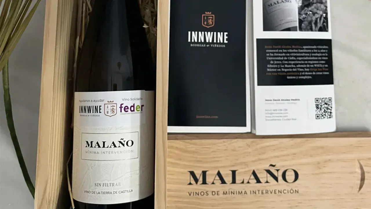 Caja de vino "Malaño" con etiqueta "Vino Solidario" y logos de INNWINE y feder. Incluye folleto informativo.