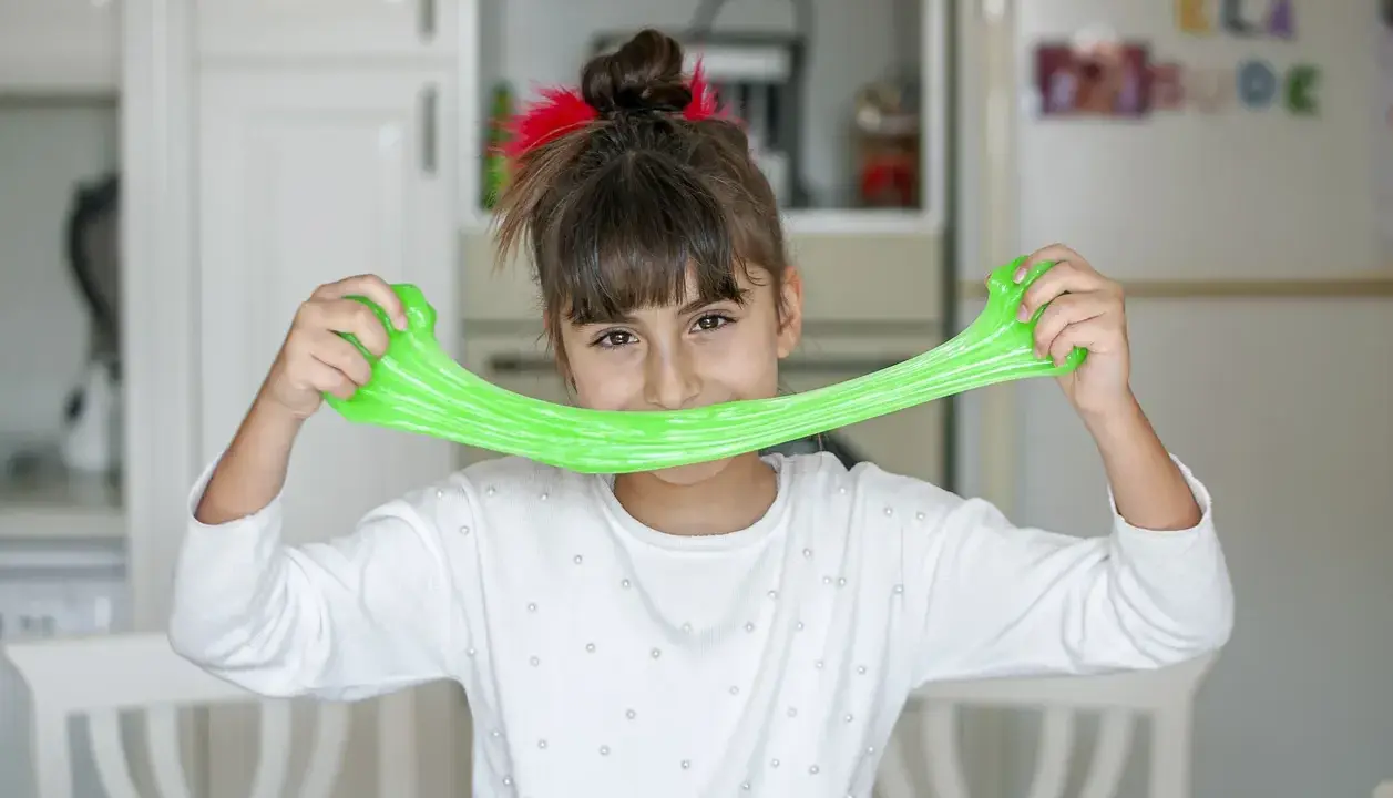 Bambina sorridente con slime verde brillante, un divertente esperimento per la ricetta slime fatta in casa.