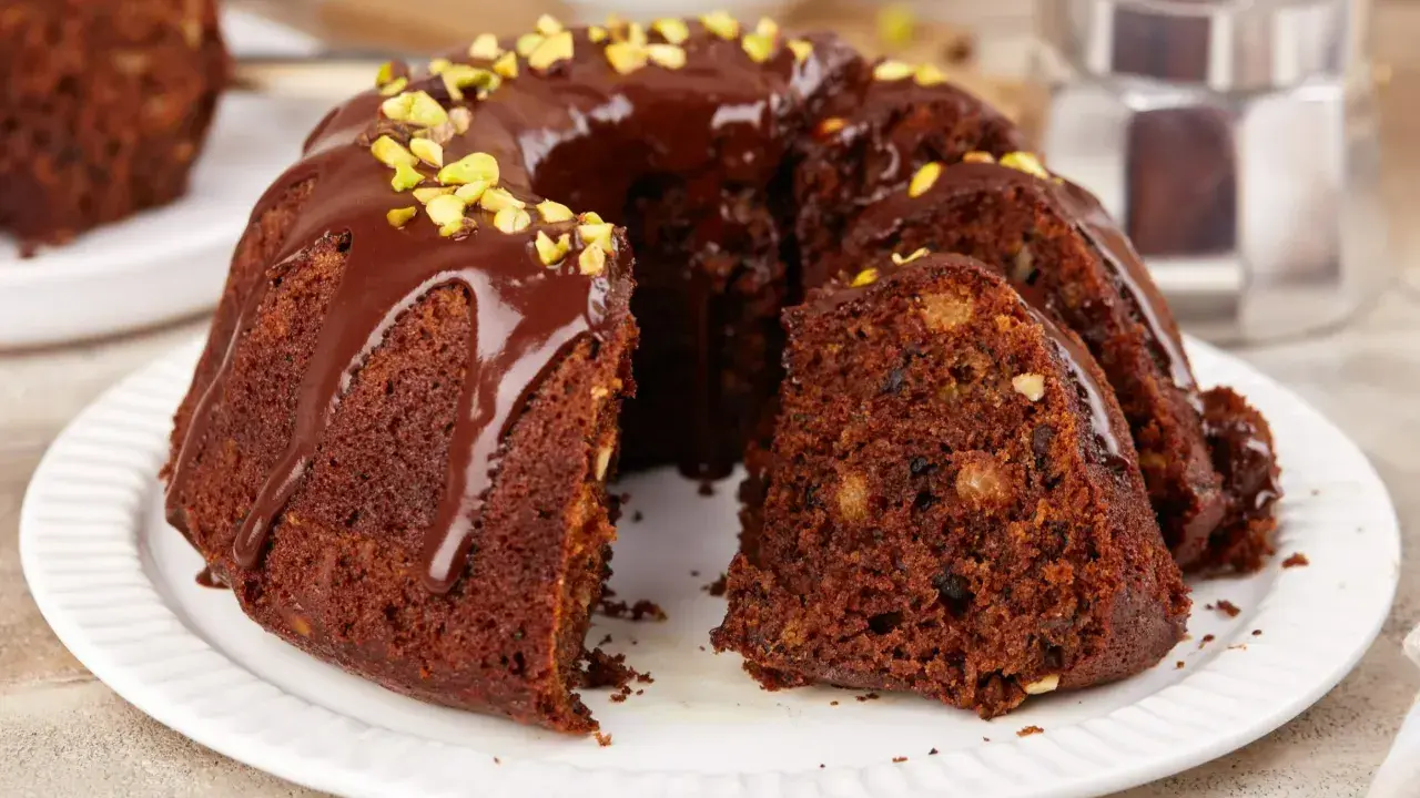 Pyszna babka na oleju, polana czekoladą i posypana pistacjami, z kawałkiem na talerzyku.