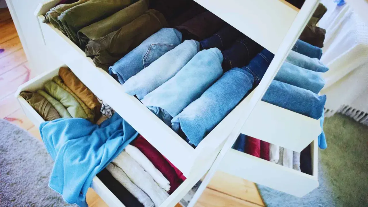 Cajones de armario organizados tras una **limpieza de armario**. Ropa doblada y ordenada por color y tipo, predominan los vaqueros y prendas en tonos tierra y azules.