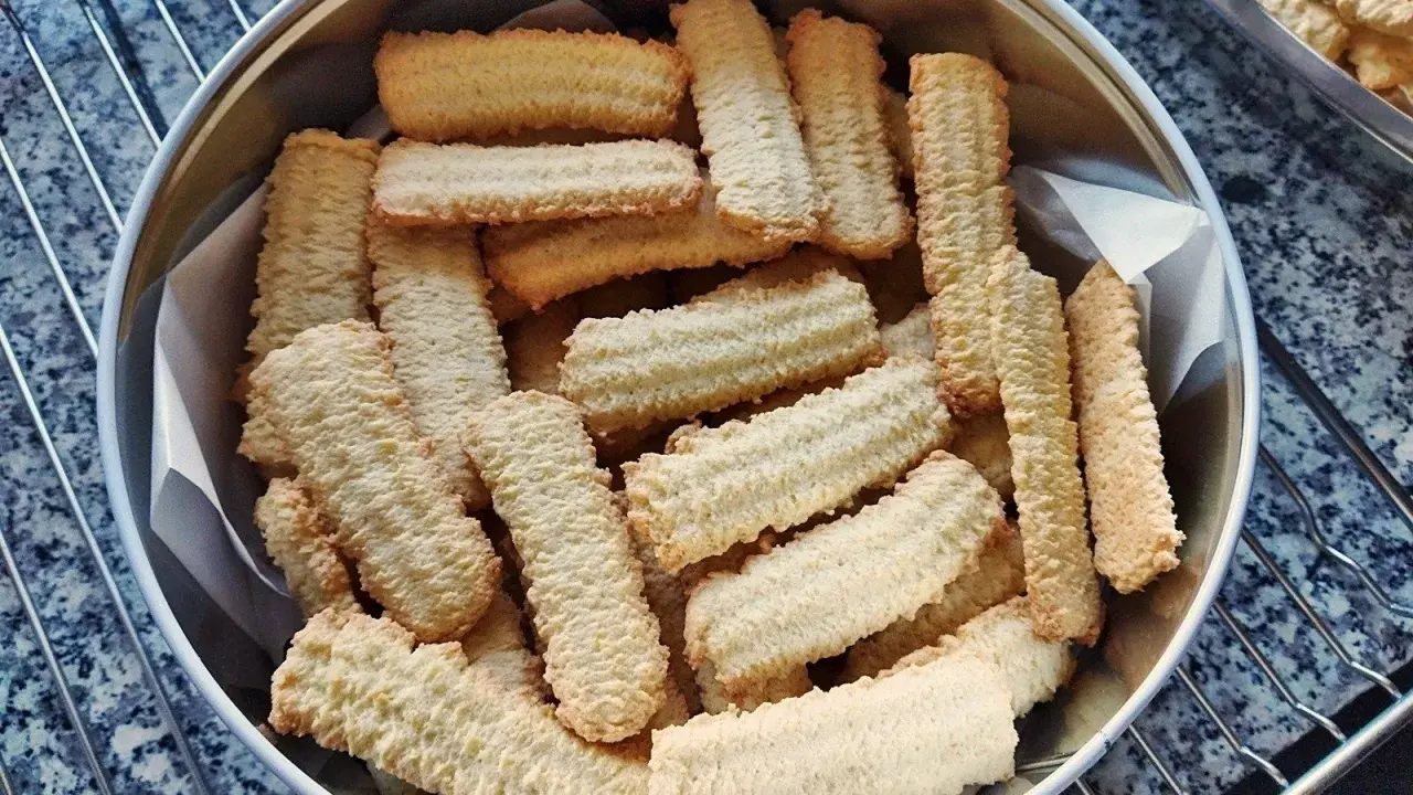 Stos pysznych, chrupiących ciastek z maszynki, ułożonych w metalowej puszce. Idealne na popołudniową herbatę.