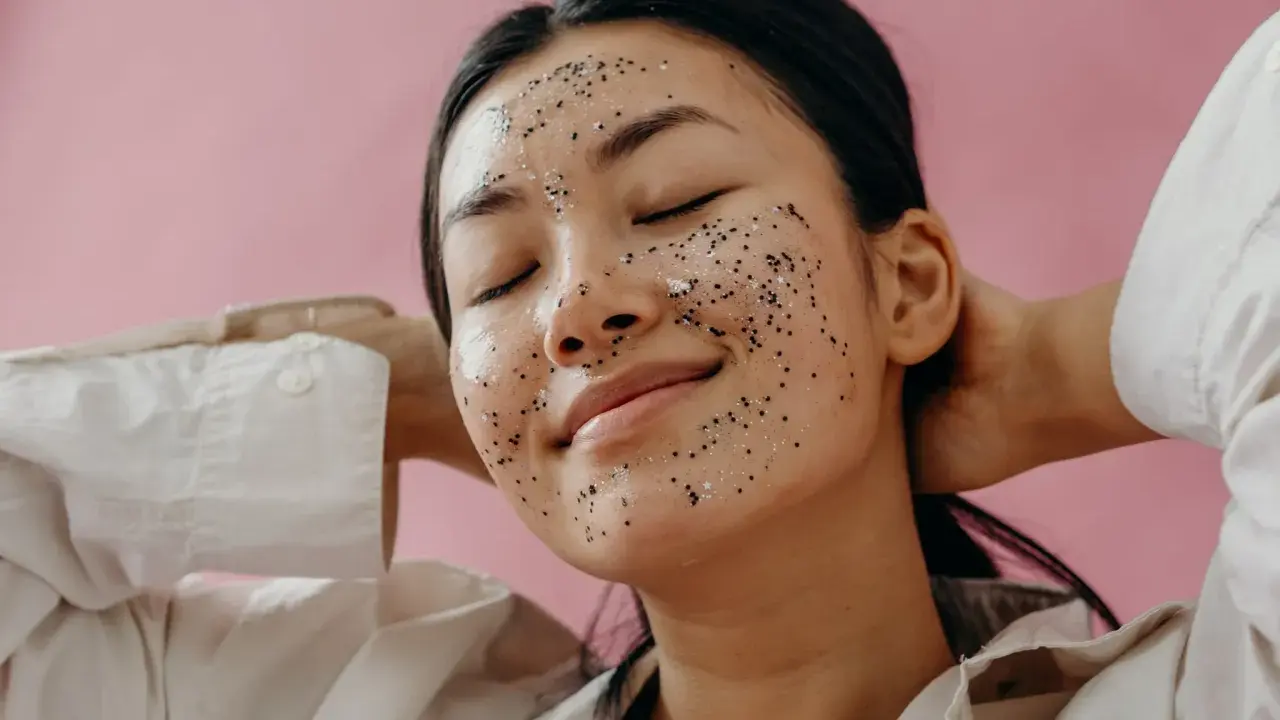 Une jeune femme au visage couvert d'un masque exfoliant scintillant, profitant d'un moment de détente. Elle nous rappelle pourquoi exfolier sa peau est essentiel pour un teint éclatant.