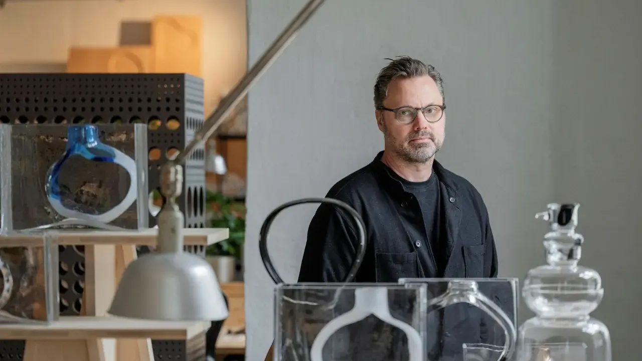 Matti Klenell, en man med glasögon, står bland sina konstverk av glas.