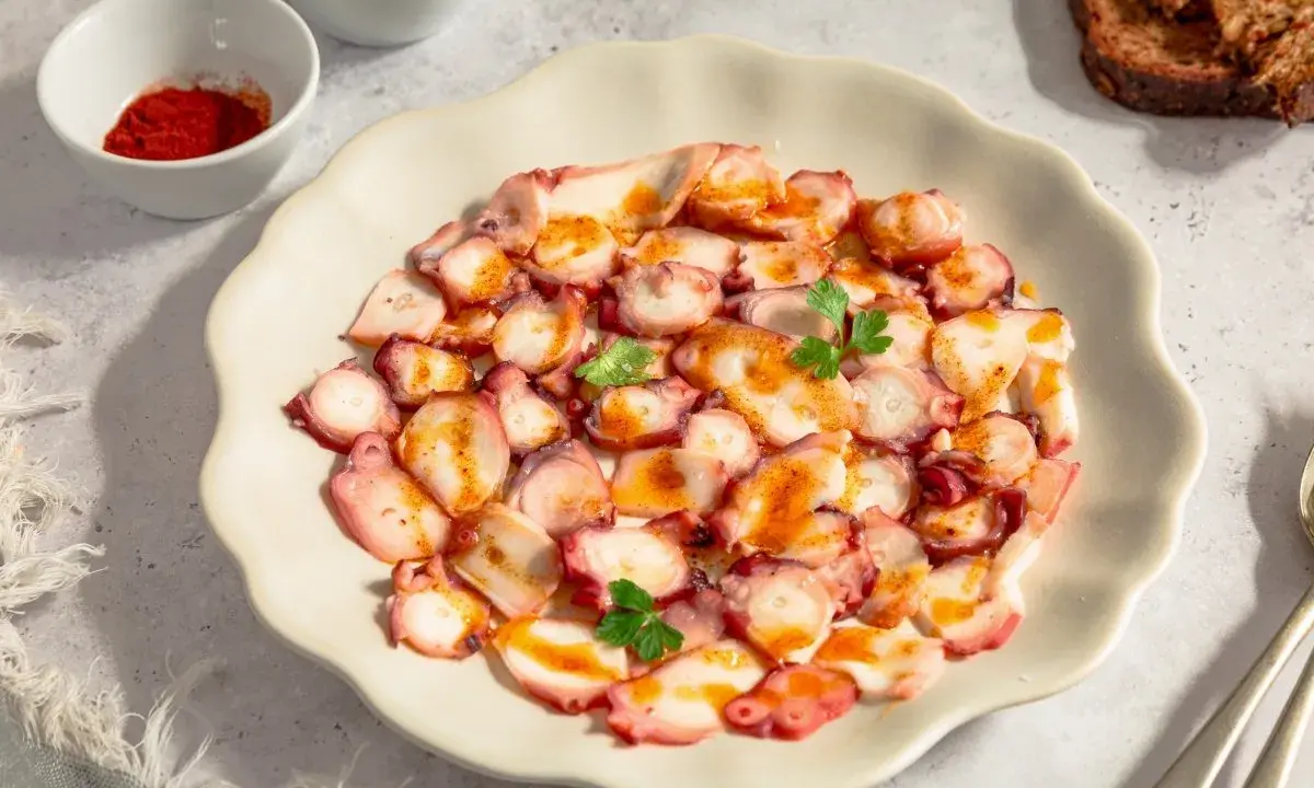 Delicioso carpaccio de pulpo, finas láminas con pimentón y perejil, servido en plato blanco.