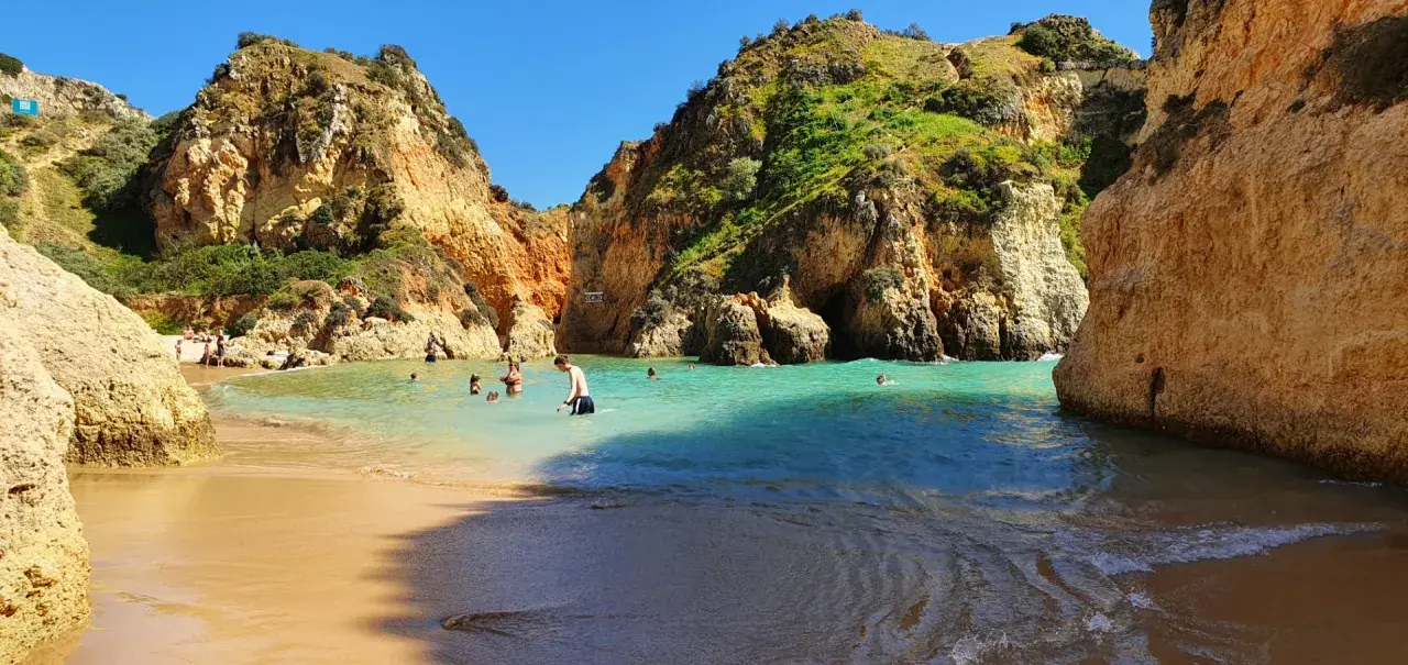 Sonnige Bucht mit Felsen und türkisfarbenem Wasser. Menschen baden und genießen das milde Wetter im **Portugal im Dezember**.