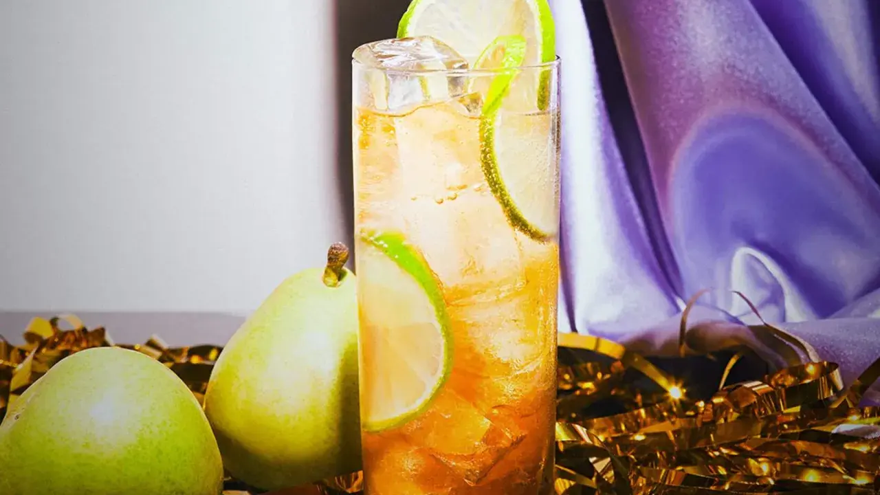 En uppfriskande drink med päron och lime, perfekt för svenska drinkar. Guldfärgad konfetti och lila tyg skapar festlig stämning.