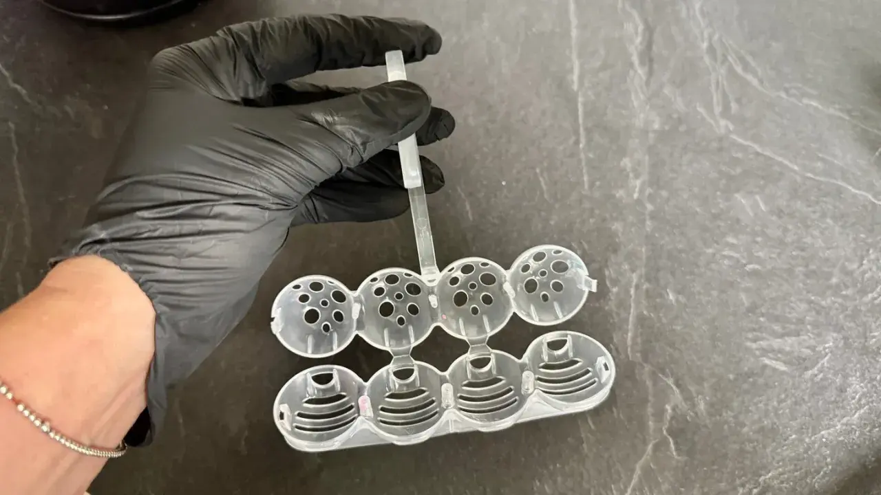 Hand in black glove holds a mold for making klostein selber machen. The mold has eight spherical compartments.