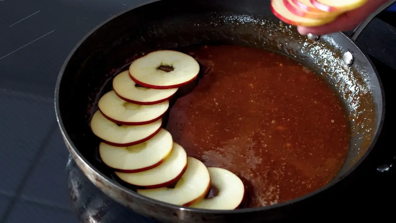 Äppelringar läggs i en panna med karamelliserad sås, förberedelse för en klassisk tarte tatin.