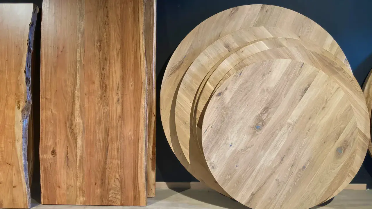Plusieurs plateaux de table ronde en bois, empilés, illustrent la définition d'une table ronde. Des planches de bois brut sont aussi visibles.