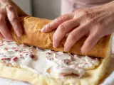 Ręce zwijają biszkopt z kremem i truskawkami. To najprostsza rolada biszkoptowa, która zachwyci smakiem.