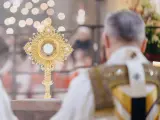 Goldene Monstranz mit Hostie im Schein von Kerzenlicht. Ein Priester in festlicher Kleidung feiert die Messe, ein Moment des weihnachtlichen Christentums.