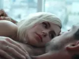 Blondynka i brunet leżą blisko siebie, ich ciała stykają się. Intymna scena, która sugeruje seks na scenie.