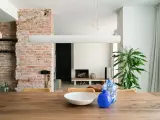 Salón con pared de ladrillo visto, mesa de madera con jarrones y planta.
