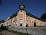 Klasztor Paradyż, okazały budynek z pomarańczowo-białą fasadą i wieżyczką, otoczony murem.
