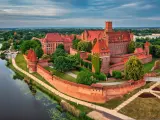 Malbork, największy zamek w Polsce, majestatycznie wznosi się nad rzeką Nogat. Czerwona cegła i strzeliste wieże tworzą imponujący widok.
