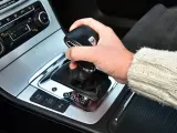 Dłoń trzyma gałkę zmiany biegów w samochodzie. Widoczna jest automatyczna skrzynia biegów DSG z przyciskami ESP, Auto Hold i czujnikami parkowania.