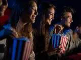 Uśmiechnięci ludzie jedzą popcorn w kinie. Idealny strój do kina to coś wygodnego, jak na przykład bluza.
