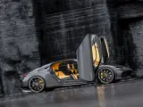 Szary Koenigsegg Gemera, czteromiejscny supersamochód z otwartymi drzwiami, prezentuje swoje żółte wnętrze na tle skalistej ściany.