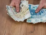 Dłonie trzymające stosy polskich banknotów 200 zł i 50 zł, być może na sześciomiesięczną odprawę emerytalną.