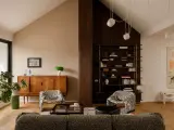 Salón acogedor con **techo inclinado interior**, muebles de madera, estanterías y sillones estampados.