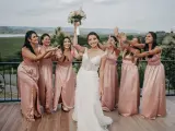 Panna młoda z bukietem wzniesionym do góry, otoczona przez uśmiechnięte druhny w różowych sukniach. Radość i wsparcie świadkowej w tym wyjątkowym dniu.