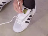 Pokazuję, jak wiązać sznurówki w adidasach Superstar. Białe sznurówki przeplatane przez czarne paski.