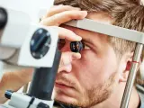 Mężczyzna podczas badania okulistycznego. Lekarz używa urządzenia do angiografii fluoresceinowej, aby zbadać jego oko.