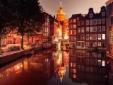 Nocny Amsterdam, kanał odbija oświetlone kamienice i kopułę kościoła. Czerwona ulica Amsterdam w blasku latarni.