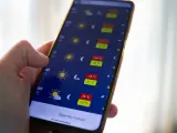 Dłoń trzyma smartfon z otwartą aplikacją pogoda, pokazującą prognozę z wysokimi temperaturami.
