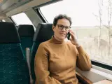 Kobieta w brązowym swetrze rozmawia przez telefon w pociągu. Czas na moją kolej, by usiąść przy oknie i podziwiać widoki.