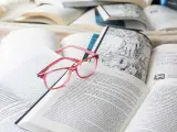 Różowe okulary spoczywają na otwartych książkach, tworząc atmosferę nauki i wiedzy. ibidem.