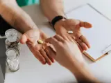 Dwie dłonie, jedna z żółtą tabletką, druga z białą. Obok buteleczki z lekami, w tym n acetylocysteina.