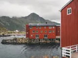 Czerwone domy rybackie nad wodą, w tle góry. Czy lecąc do Norwegii potrzebny jest paszport? Tak, jeśli nie jesteś obywatelem UE/Schengen.