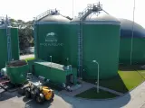 Zielone zbiorniki instalacji biogazowej, z logo "DYNAMIC BIOGAS MADE IN POLAND". Obok ładowarka i kontener.
