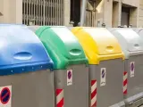 Fila de contenedores de reciclaje de Ecoembes en la calle: azul, verde, amarillo y grises.