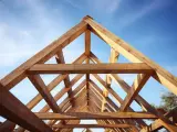 Drewniana więźba dachowa dwuspadowa tworzy geometryczny wzór na tle błękitnego nieba.