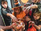 Barn i Halloween-kostymer sträcker sig efter godis ur en korg. Det är en klassisk "bus eller godis"-kväll!