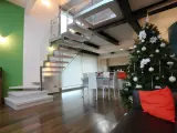 Un moderno soppalco casa con scala in vetro e legno, albero di Natale addobbato e un divano con cuscino arancione.