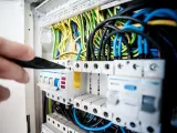Ręka majstruje przy bezpiecznikach. Kolorowe przewody tworzą skomplikowaną instalację elektryczną.