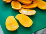 Pokrojone w łódeczki, soczyste mango w intensywnym kolorze, jakby w ciąży z owocową obfitością, leżą na zielonej desce.