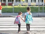 Dwie dziewczynki z plecakami idą za rękę przez pasy. Od ilu lat dziecko może samo chodzić po mieście?