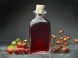Prosta nalewka z dzikiej róży w szklanej butelce, otoczona świeżymi owocami dzikiej róży.